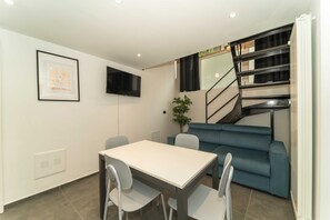 Una sala de estar moderna con un sofá, una mesa de comedor con sillas, un televisor montado en la pared y una escalera.