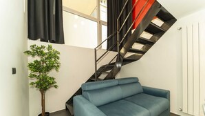 A modern living area with a blue sofa, a staircase with a red accent, and a potted plant.