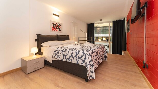 A bedroom with a bed, bedside table, and a red wall.