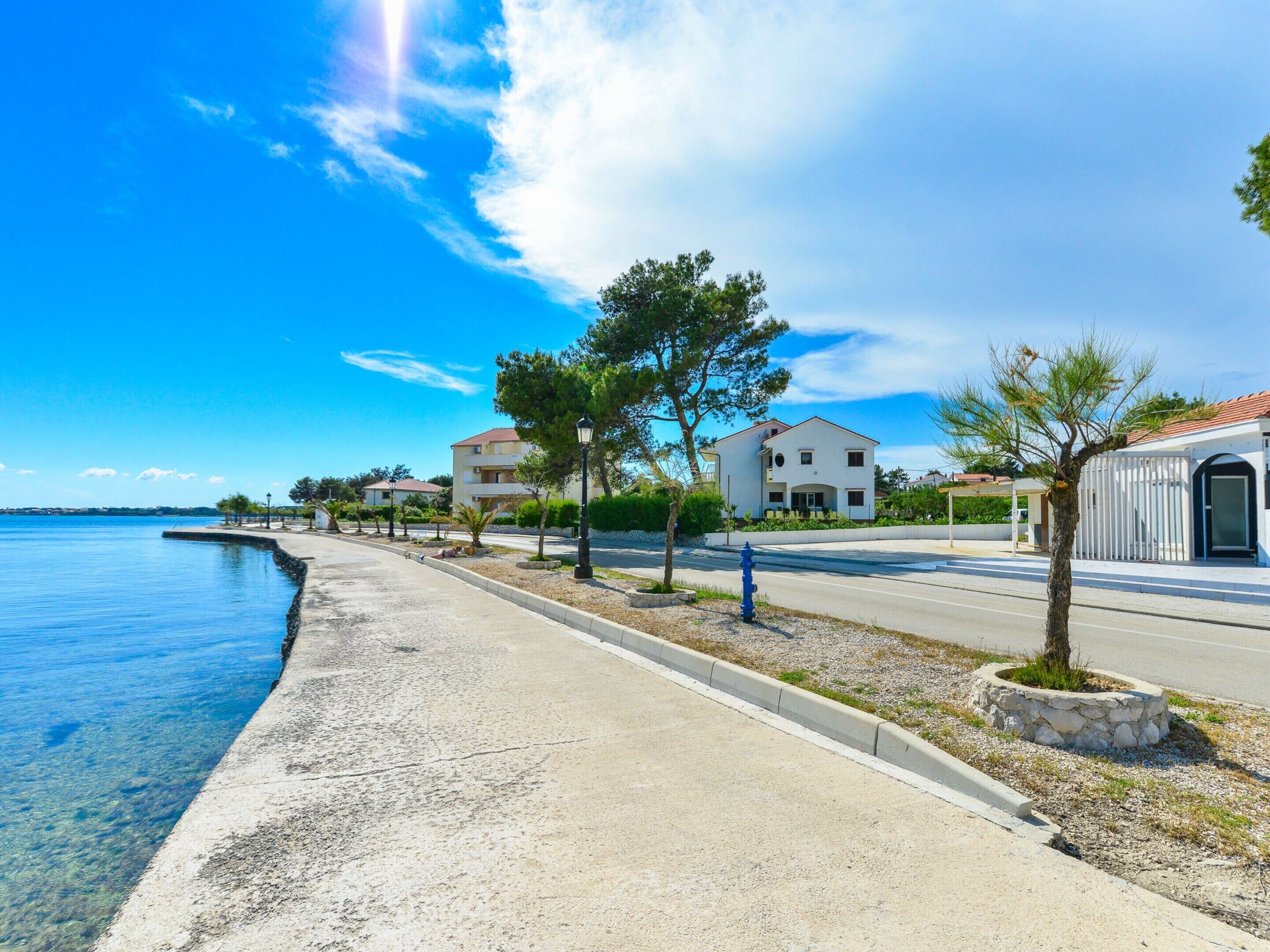 A coastal road with houses, clear skies, and a calm sea.