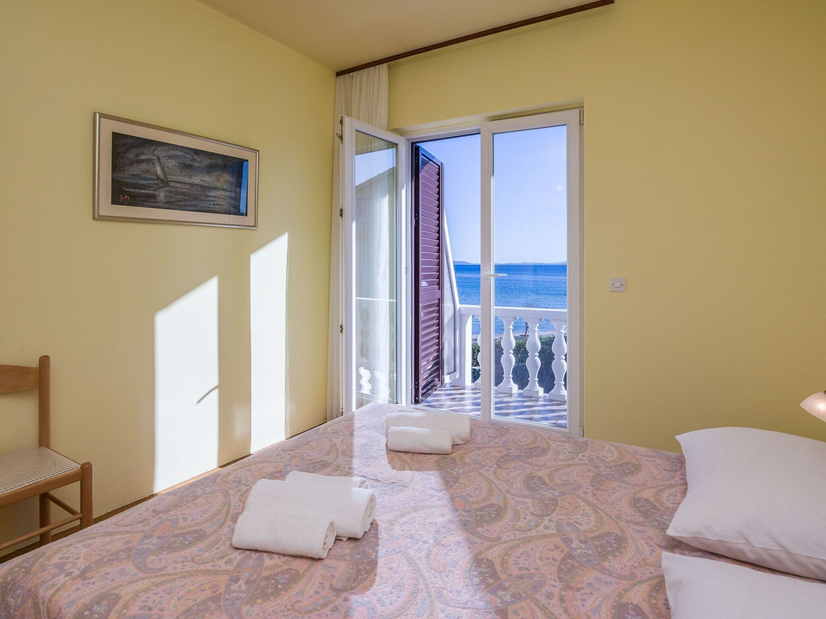 Ein Schlafzimmer mit Bett, Stuhl, Gemälde und einem Balkon mit Meerblick.
