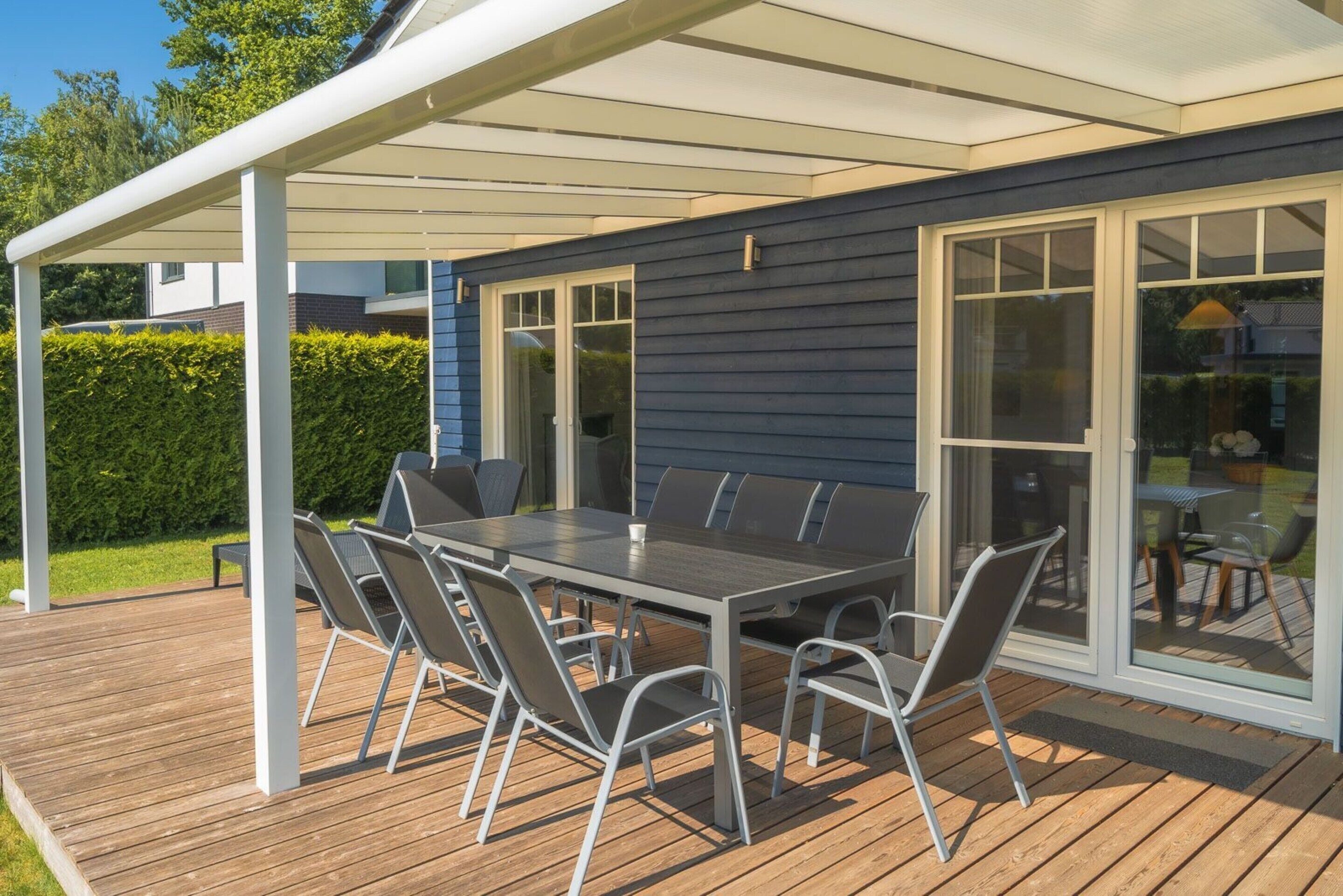 Eine überdachte Terrasse mit Tisch und Stühlen, großen Schiebeglastüren und einem Holzboden.