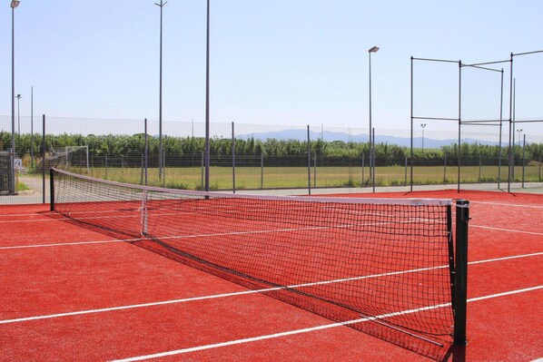 A tennis court with a net, surrounded by a fence and street lamps.