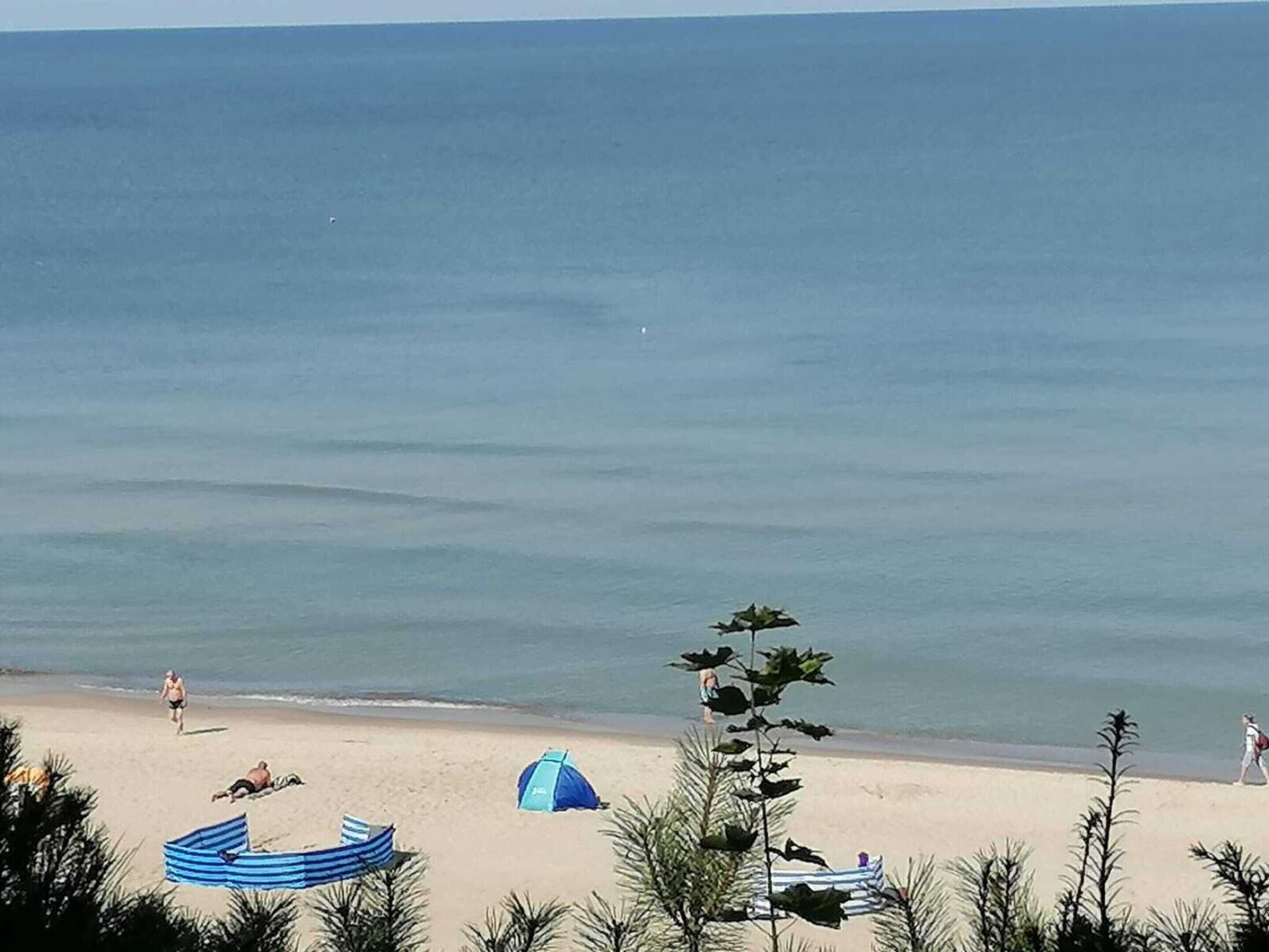 Une plage avec une tente, un auvent à rayures et quelques personnes qui se promènent.