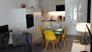 A modern living space with a sofa, dining table, chairs, and a kitchen area. - Apartment Near Baltic Sea With Balcony View (Rewal)