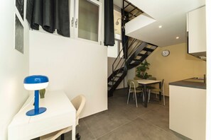 A compact kitchen with a dining area, a staircase, and a clock on the wall.