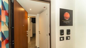 Un couloir d’hôtel avec une porte en bois, une affiche de Mars accrochée au mur et une série d’interrupteurs noirs.