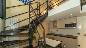 Une cuisine moderne dotée d’un four encastré, un coin repas avec une table et des chaises, et un escalier avec des rampes en métal.