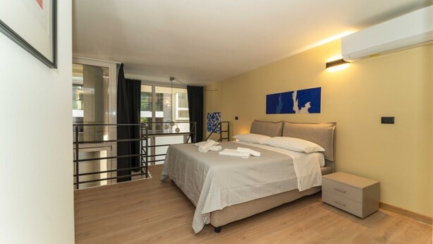 Une chambre à coucher comprenant un lit, une table de chevet, un climatiseur fixé au mur et une fenêtre donnant sur un paysage agréable.