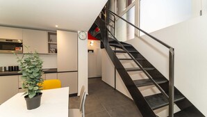 A modern kitchen with a built-in oven, a dining area with a white table and a potted plant, and a staircase with a metal railing leading to an upper level. - GuestHost - Galaxy Lofts - Appt Saturn x4 (Torino)
