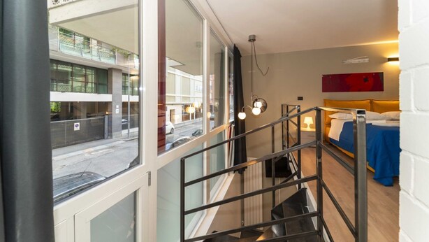 A modern hotel room with a balcony, a staircase, and a bed with a blue bedspread. - GuestHost - Galaxy Lofts - Appt Saturn x4 (Torino)