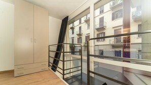 Habitació amb sòl de fusta, armari amb portes corredisses, balcó de vidre amb barana metàl·lica i vista d'un edifici amb balcons.