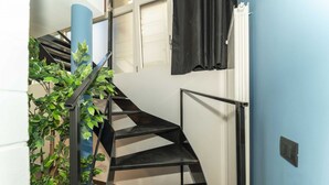 Una escala espiraltra amb barana metàl·lica, una planta en test i una paret blava.