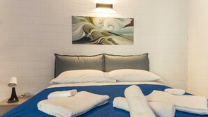 Habitació d'hotel amb un llit, almoines, una obra d'art penjada a la paret i una tauleta de nit amb una làmpada.