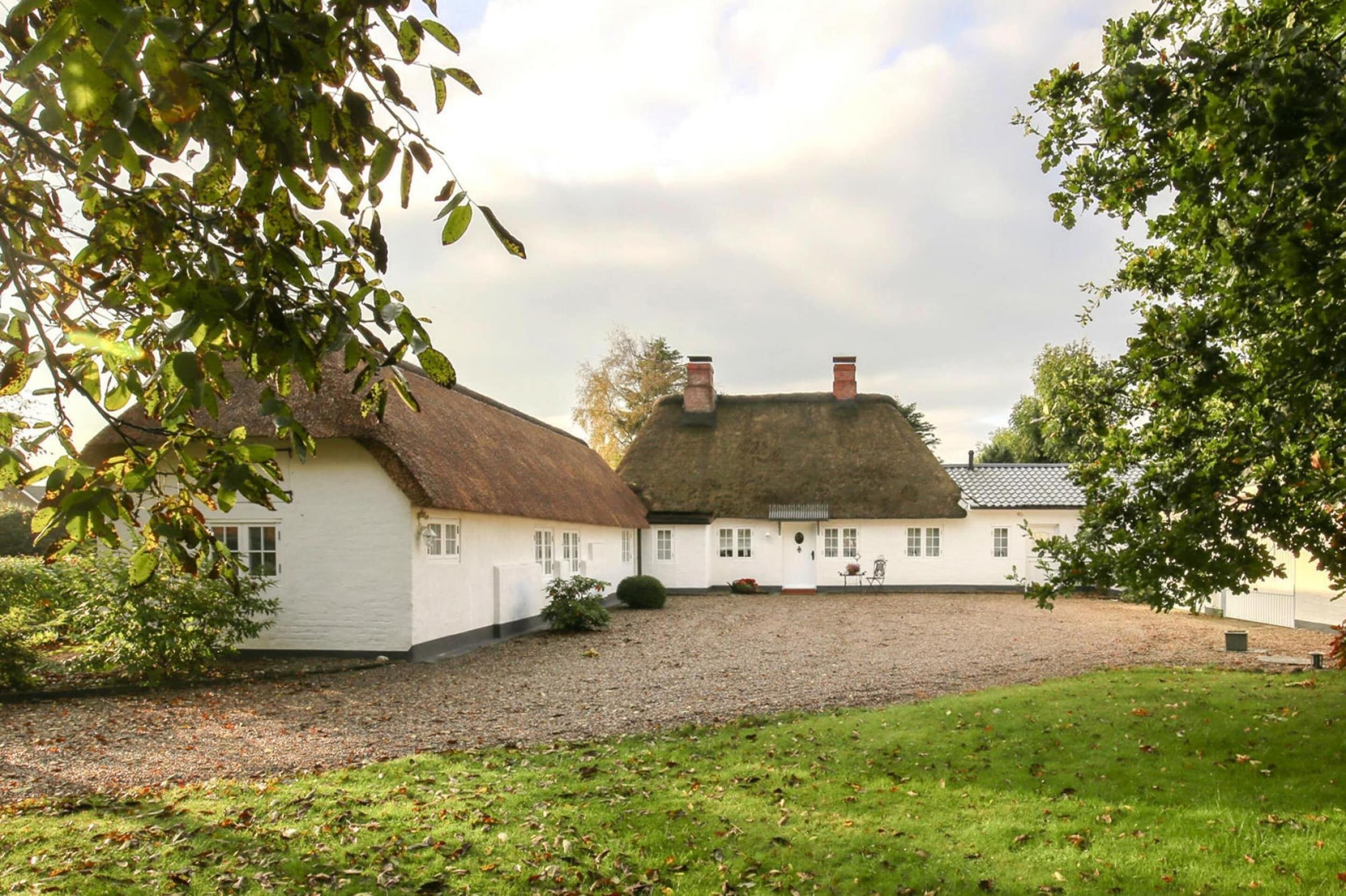 A traditional white building with a thatched roof, surrounded by a gravel driveway and a grassy area.