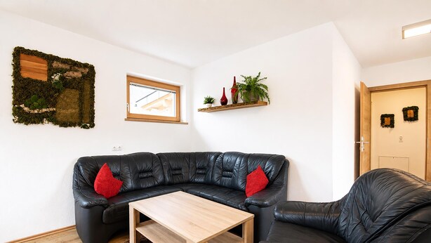 Una sala de estar moderna con un sofá de cuero negro, una mesa de centro de madera y una planta pequeña en un estante.
