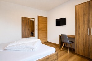 Une chambre à coucher comprenant un lit, un bureau, une chaise, un téléviseur et des armoires en bois.