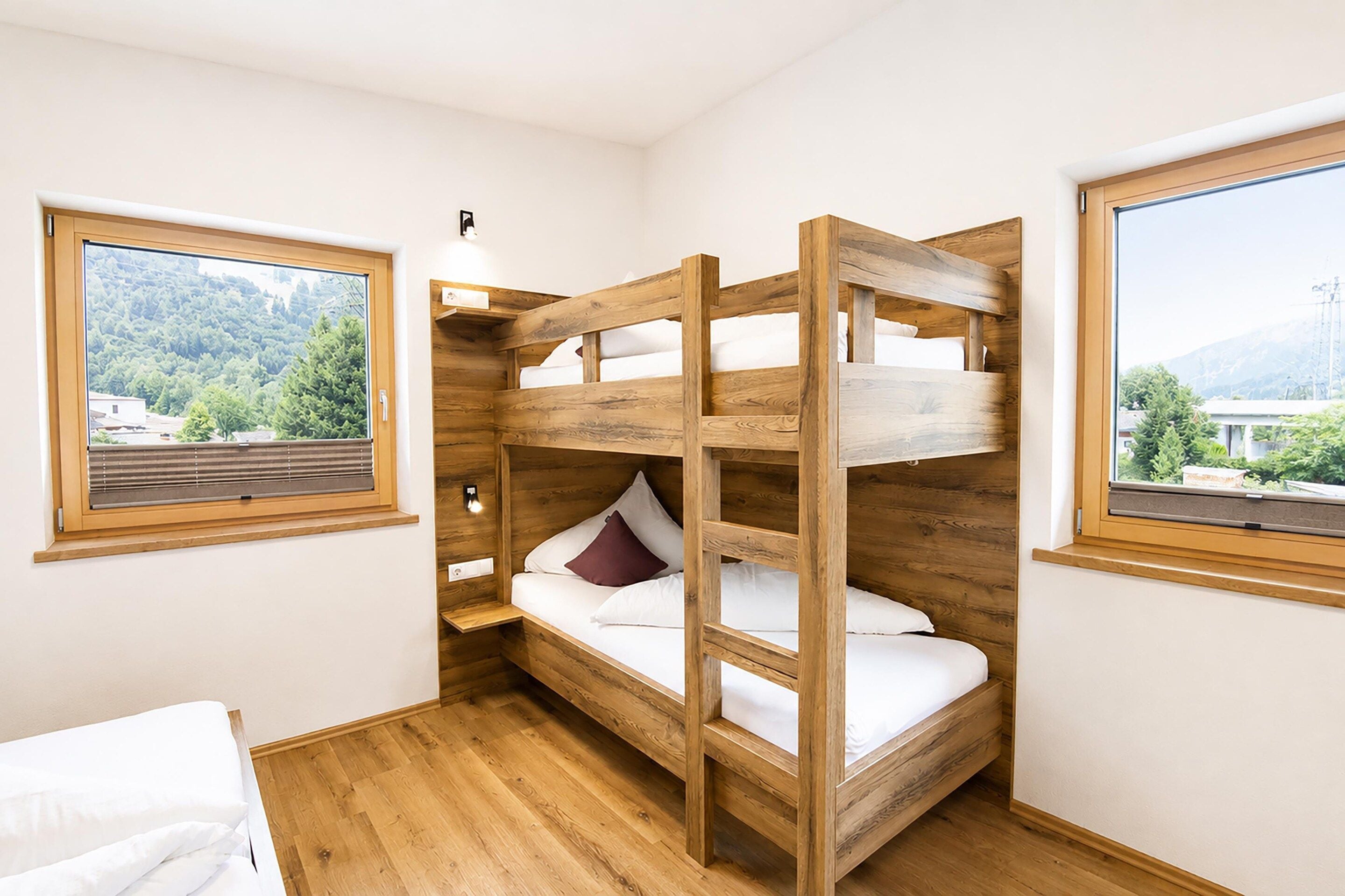 A bunk bed room with wooden construction, a window with a view of a forest, and a bedside table.