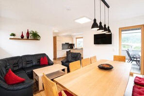 A modern living space with a black leather sofa, a wooden dining table, and a kitchen in the background. - Holiday Home in Aschau Near Climbing Center (Aschau Im Zillertal)