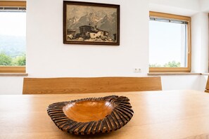 A dining table with a wooden bowl centerpiece, a framed painting on the wall, and windows with a view of greenery. - Holiday Home in Aschau Near Climbing Center (Aschau Im Zillertal)
