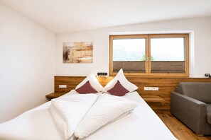 Ein Hotelzimmer mit einem Bett, einem Holz-Kopfteil, einem grauen Sofa, einem Fenster mit Jalousien und einem Wandbild.