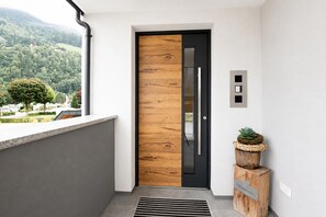 A modern entrance with a wooden door, a small plant on a wooden stand, and a view of a green landscape. - Holiday Home in Aschau Near Climbing Center (Aschau Im Zillertal)