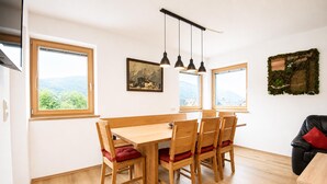 Un comedor con mesa y sillas de madera, un cuadro en la pared y grandes ventanales con vistas al exterior.