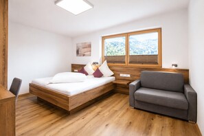 A modern bedroom with a wooden bed, a gray armchair, and a window with a forest view. - Holiday Home in Aschau Near Climbing Center (Aschau Im Zillertal)