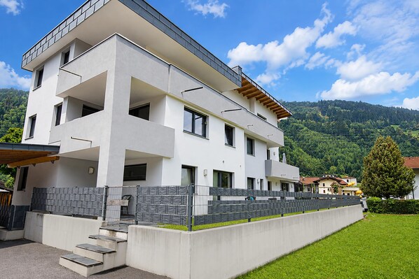 Een modern appartementencomplex met meerdere verdiepingen, een plat dak, grote ramen en een betonnen trap die naar de ingang leidt.