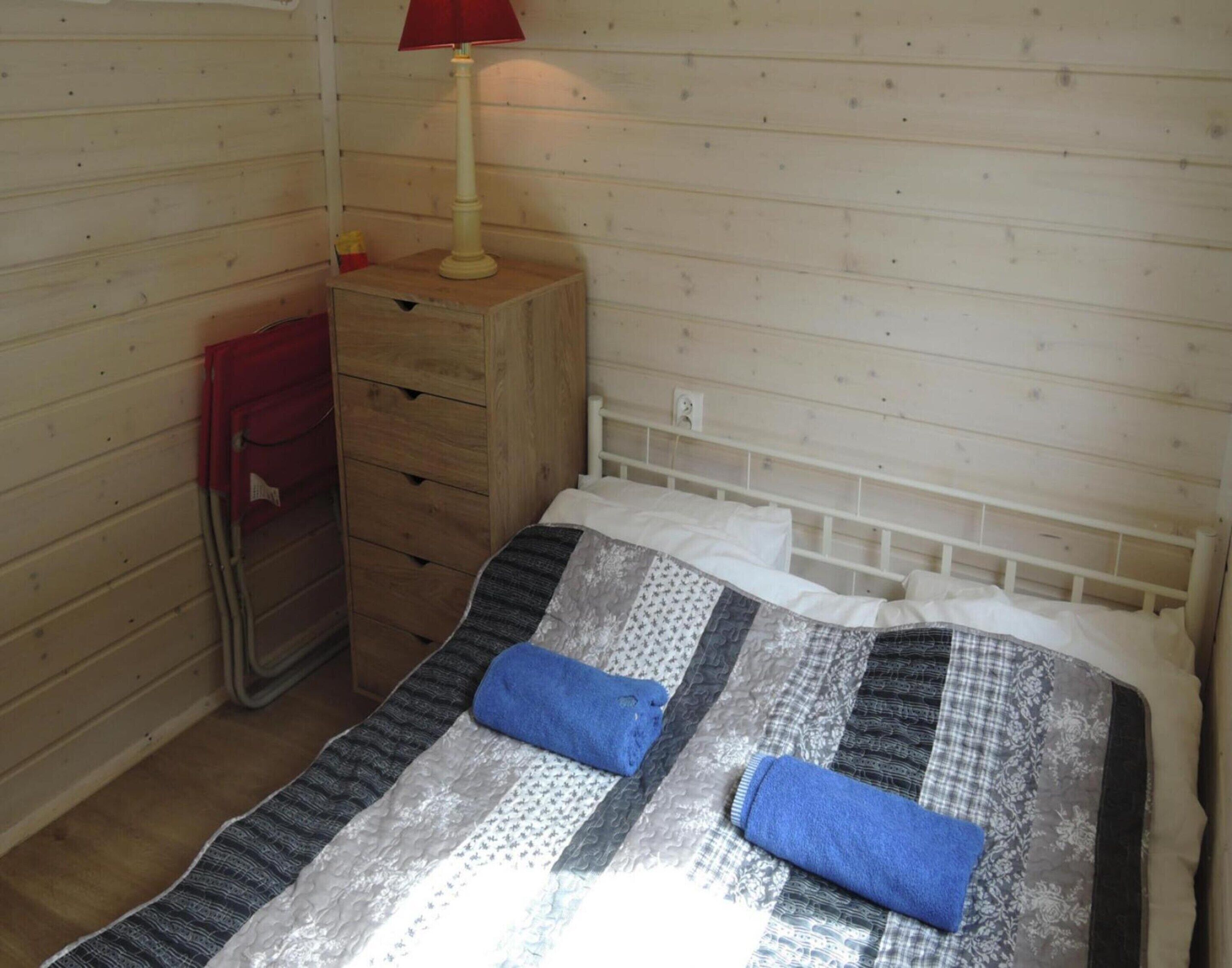 Una habitación pequeña y acogedora, con una cama de madera, una mesita de noche con lámpara y un aparador.