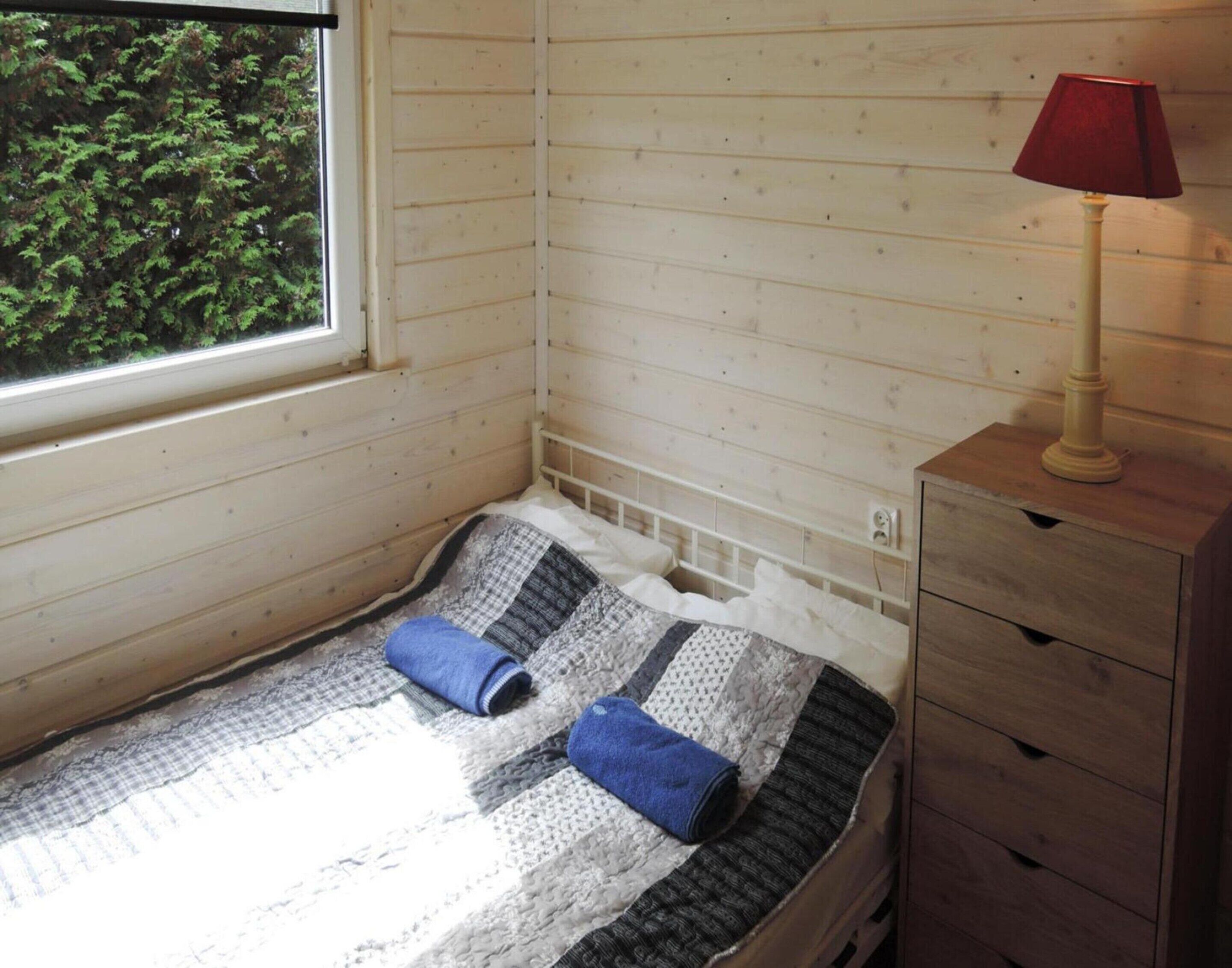 Une petite pièce agréable et chaleureuse, avec un lit simple, une commode en bois et une fenêtre donnant sur les arbres.