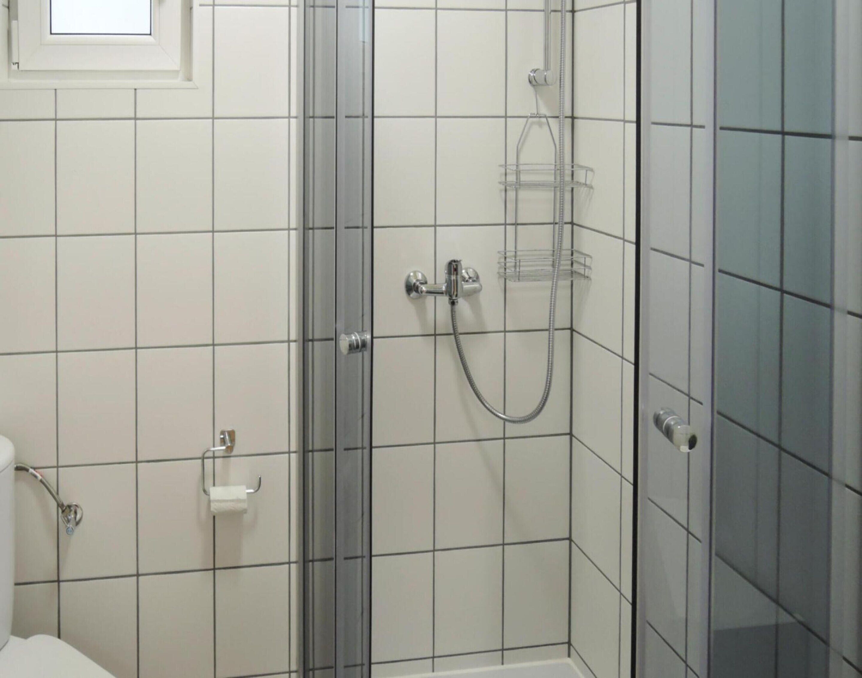 Ein Badezimmer mit Duschkabine aus Glas, weißen Fliesen und einer Toilette.