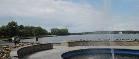 A circular fountain with water jets, surrounded by a paved walkway and flower beds.