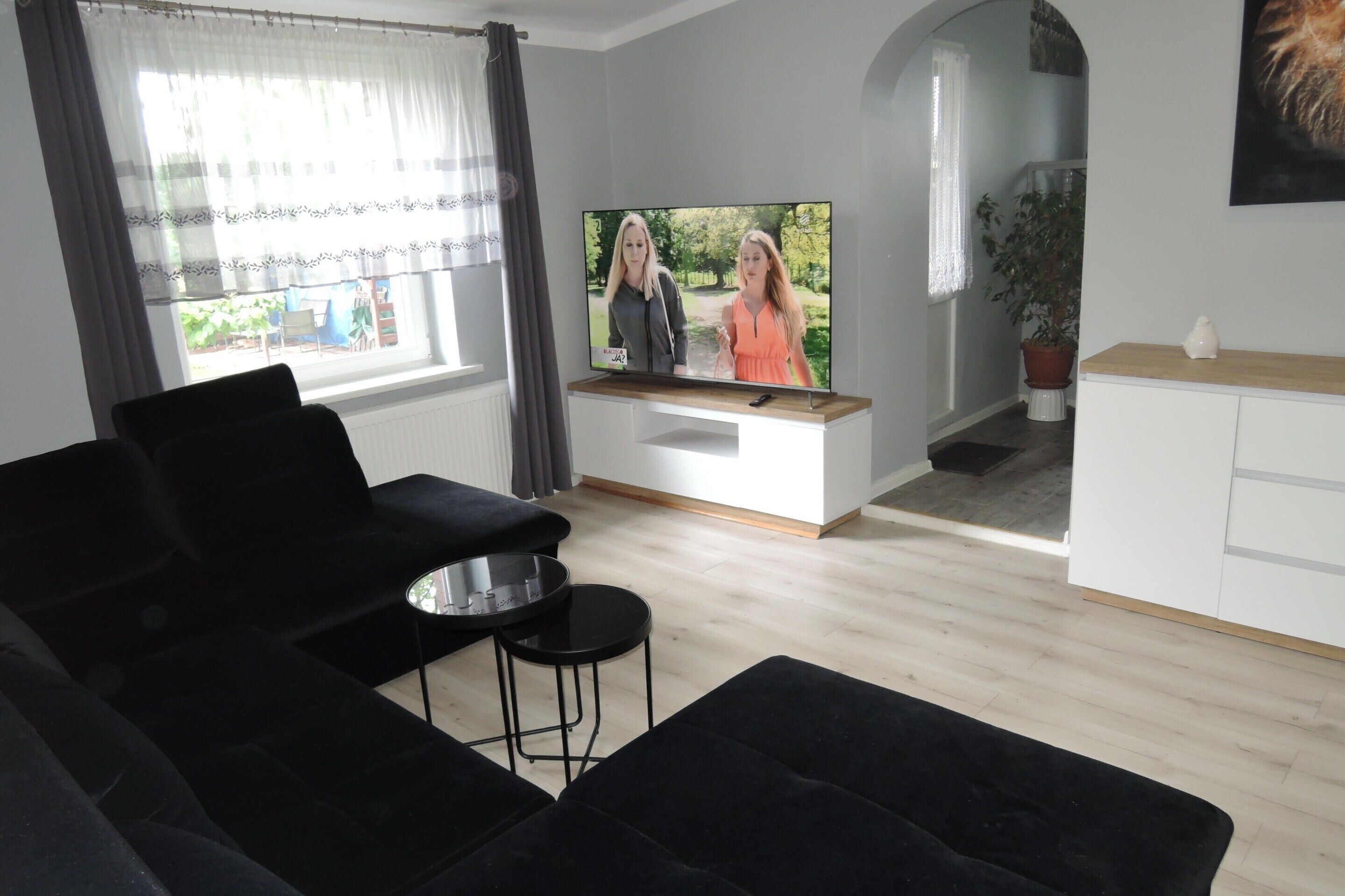 Ein modernes Wohnzimmer mit einem schwarzen Sofa, einem kleinen runden Tisch, einem Flachbildfernseher und einem Blumentopf.