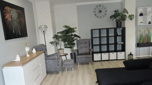 Uma sala de estar moderna com um sofá cinzento, um sofá preto, uma poltrona cinzenta, uma mesa pequena e uma grande planta em vaso.