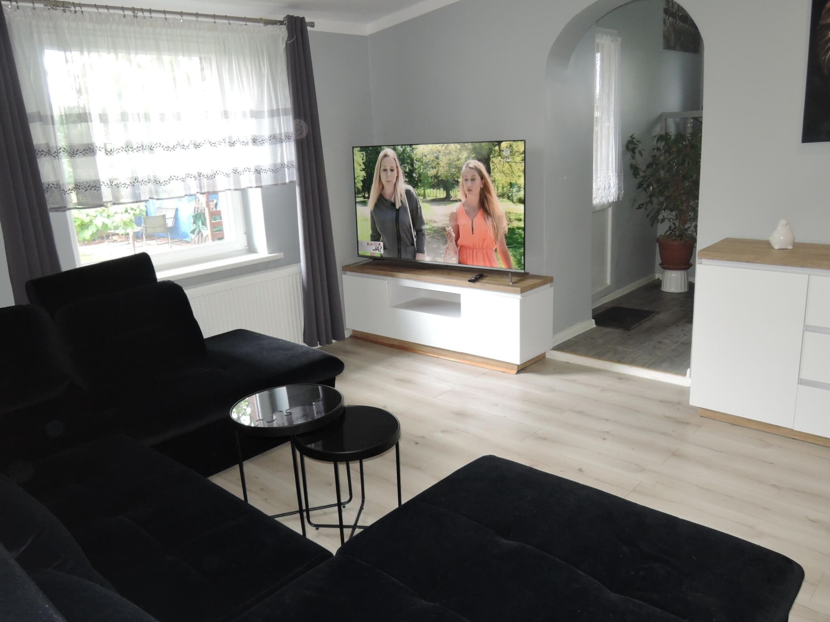 Ein modernes Wohnzimmer mit Flachbildfernseher, schwarzen Sofas und einem kleinen Couchtisch.
