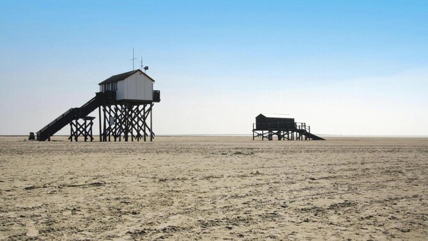 A beach with two wooden structures, one with a staircase and another with a flat roof. - Ferienwohnung in St. Peter-ording (St. Peter-Ording)