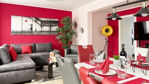 A modern living room with a grey sofa, red cushions, a dining area with red chairs, a large mirror, and a television. - Holiday Home in Walkenried With Sauna (Walkenried)