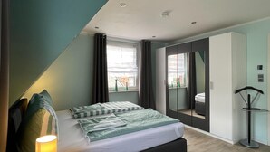 A modern bedroom with a bed, a bedside table, a lamp, a wardrobe, and a mirror. - Holiday Home in Walkenried With Sauna (Walkenried)