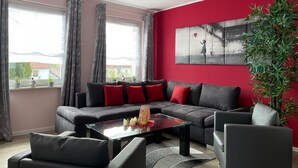 A modern living room with a sectional sofa, a glass coffee table, and a red accent wall. - Holiday Home in Walkenried With Sauna (Walkenried)