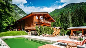 A wooden cabin with a pool, outdoor seating, and a mountain backdrop. - Hideway Chalet Gamsgluck With Pool and Sauna (Waidring)