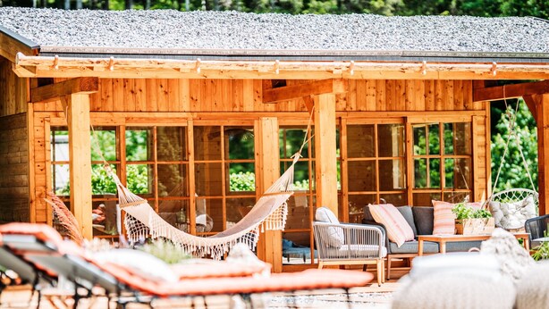 A wooden cabin with a covered patio, outdoor seating, and a hammock. - Hideway Chalet Gamsgluck With Pool and Sauna (Waidring)