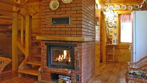 A rustic cabin interior with a brick fireplace, wooden walls, and a dining area with a table and chairs. - Fenced Cottage in the Middle of Nature, Right by the Lake, Rentyny (Gietrzwald)