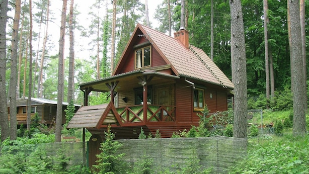 A rustic cabin with a steeply pitched roof, wooden exterior, and a porch with a railing. - Fenced Cottage in the Middle of Nature, Right by the Lake, Rentyny (Gietrzwald)