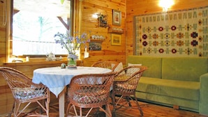 A cozy room with a round table, wicker chairs, a green sofa, wooden walls, and a floral tapestry. - Fenced Cottage in the Middle of Nature, Right by the Lake, Rentyny (Gietrzwald)
