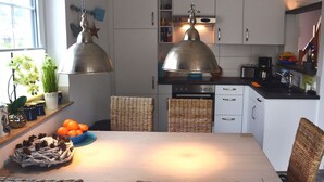 A modern kitchen with white cabinets, a dining table, wicker chairs, and pendant lights. - Doppelhaushalfte Dock No. 7.0 in Zirchow (Zirchow)