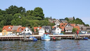 A waterfront with boats docked, houses with red roofs, and a hill with trees in the background. - Doppelhaushalfte Dock No. 7.0 in Zirchow (Zirchow)