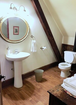 Un bagno con un lavandino su piedistallo, un water, uno specchio con cornice dorata e un pavimento in legno.