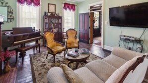 A living room with a piano, two armchairs, a sofa, a television, and a bookshelf.