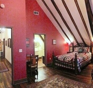 Una camera da letto con un soffitto spiovente, un letto con copripiumino decorato e una piccola sedia.